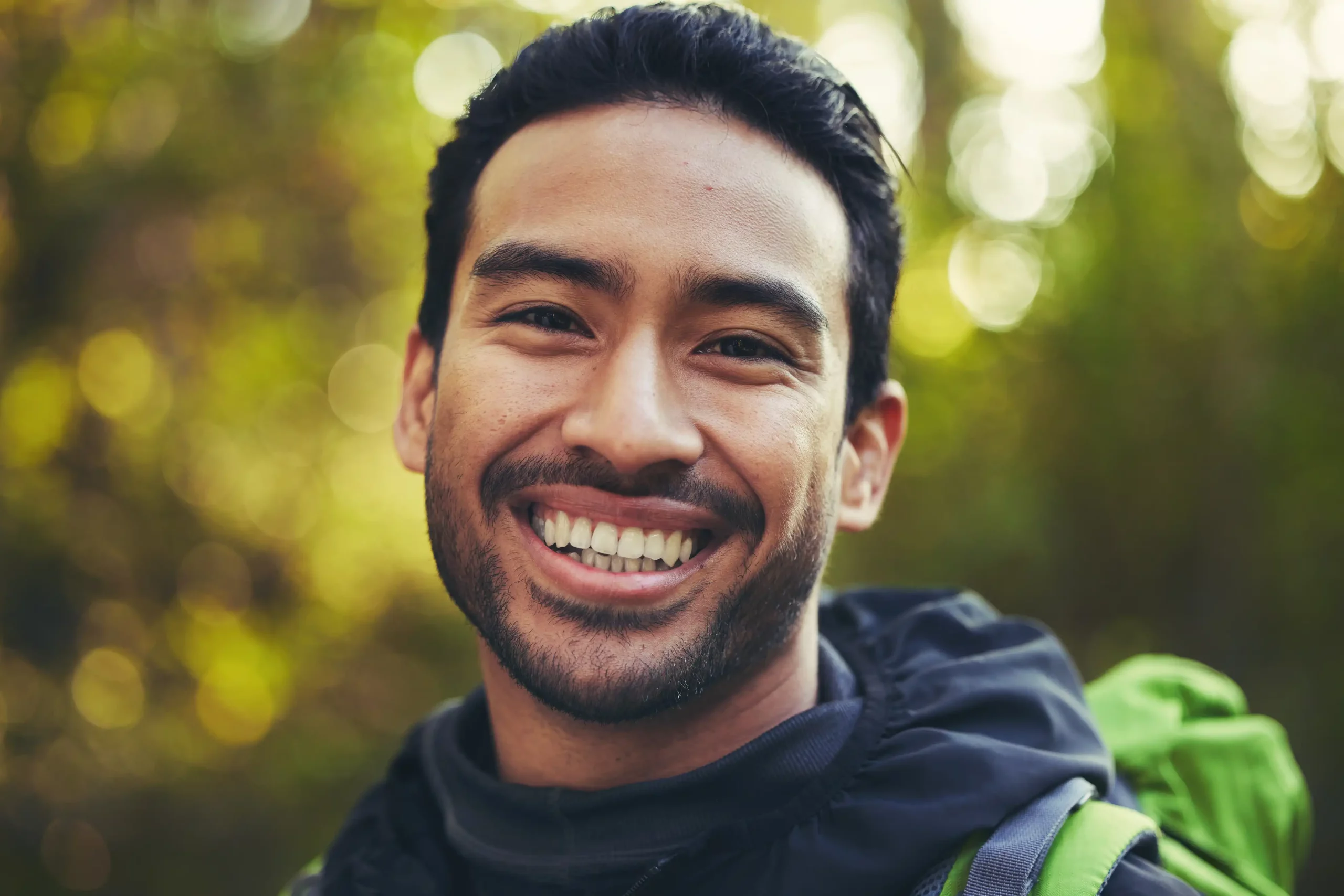 A smiling man with a backpack in the woods.