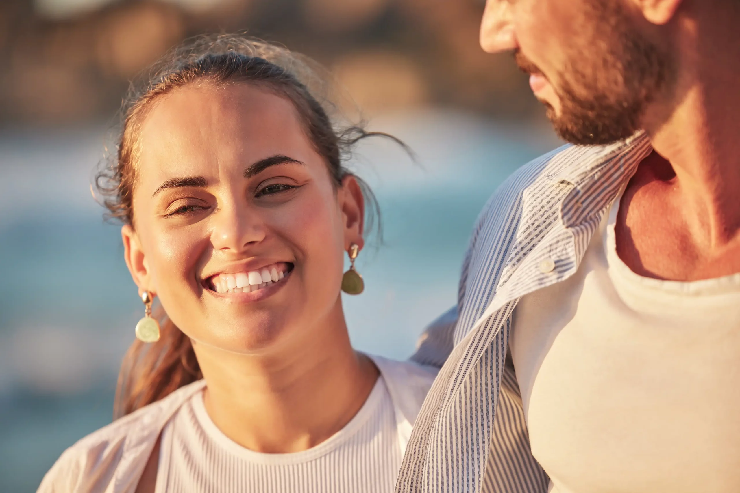 A man and woman smiling at each other on the beach.