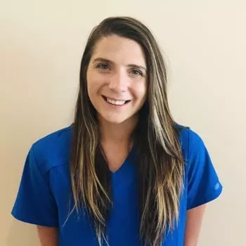 A smiling woman in a blue scrub shirt receiving TMS Therapy.